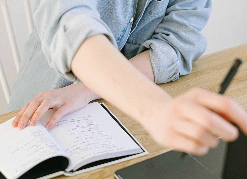 Hands beside an open notebook on a wooden table.